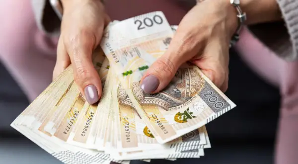 Dłonie trzymają stos banknotów 200 zł. Czy to zapowiedź sankcji kredytu darmowego?