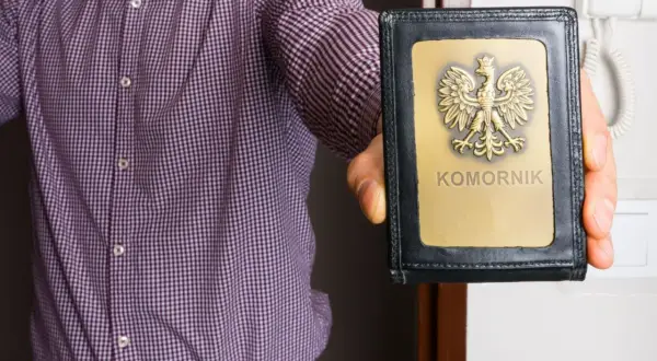 Mężczyzna w koszuli prezentuje legitymację z orłem i napisem "KOMORNIK". Może to oznaczać egzekucję komorniczą.