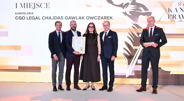 Pięć osób w strojach formalnych pozuje do zdjęcia na tle sceny z grafiką i napisem "I MIEJSCE".