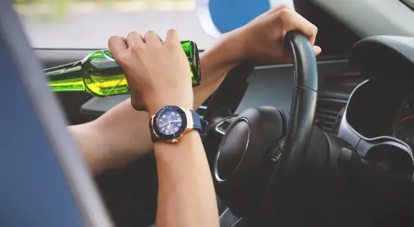 Ręce na kierownicy, jedna trzyma butelkę piwa. Ryzykowne zachowanie, stan po użyciu alkoholu.