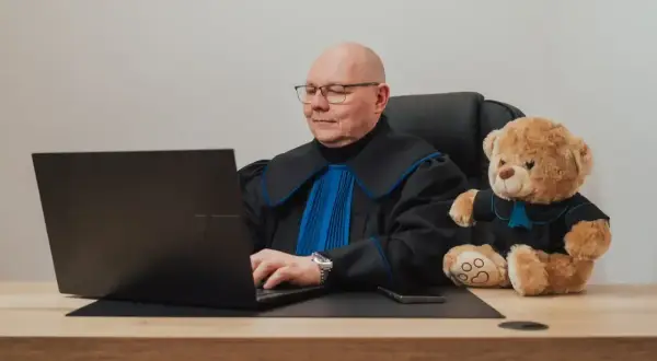 Sędzia z pluszowym misiem przy laptopie. Zastanawiasz się, ile kosztuje porada prawna u notariusza?