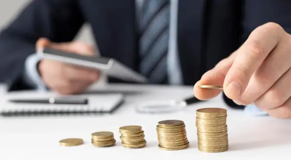 Dłoń kładzie monetę na rosnącej stercie, symbolizując zabezpieczenie alimentów i budowanie finansowej przyszłości.