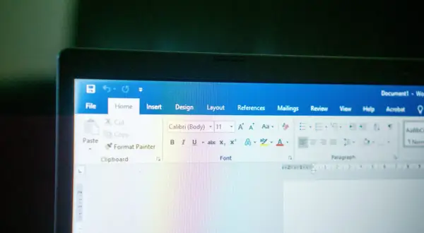 Ekran laptopa z otwartym edytorem tekstu. Widoczna jest wstążka z opcjami, w tym czcionka Calibri.