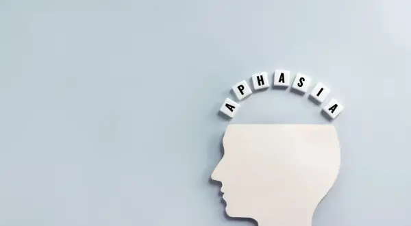 Biały profil głowy z literami tworzącymi słowo "APHASIA" nad nim. Obraz symbolizuje, co to jest afazja – trudności z mową i rozumieniem.