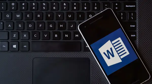Smartfon z ikoną Worda leży na klawiaturze. Możesz kliknąć ten hiperłącze, aby otworzyć dokument.
