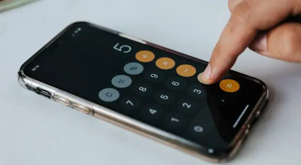 Dłoń wpisuje liczby na kalkulatorze w telefonie. Obliczenia mogą dotyczyć darowizny a zachowek.