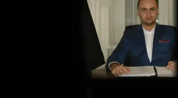 Mężczyzna w niebieskiej marynarce siedzi przy biurku z dokumentami.