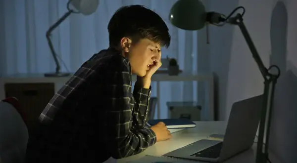 Chłopiec przy biurku, zrezygnowany, zmęczony. Czyżby padł ofiarą cyberprzemocy?