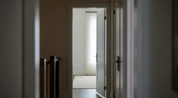 Korytarz z otwartymi drzwiami, sugerującymi naruszenie miru domowego. W tle jasne zasłony i dywan.