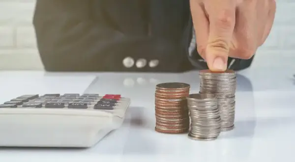 Ręka układa monety na stosie, obok kalkulatora. Zastanawiasz się, ile kosztuje sprawa o zasiedzenie u adwokata?