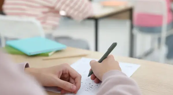 Uczeń pisze test, skupiony na zadaniach. To ważny moment, jak egzamin dojrzałości.