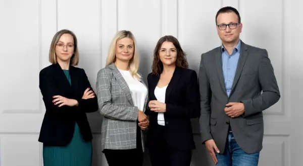 Cztery osoby w strojach biznesowych stoją obok siebie na jasnym tle.