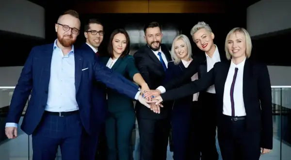 Zespół prawników w garniturach z rękami złożonymi na środku.