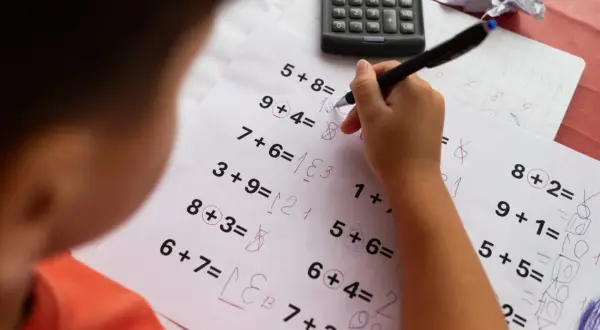 Dziecko rozwiązuje zadania matematyczne, które mogą być częścią dyskalkulia testu. Widoczny jest arkusz z działaniami i kalkulator.