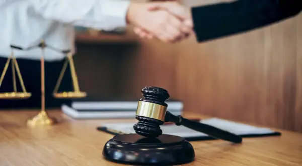 Młotek sędziowski i waga sprawiedliwości symbolizują prawo. Uścisk dłoni sugeruje porozumienie, być może w kontekście odpowiedzialności subsydiarnej.