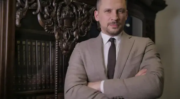 Mężczyzna w garniturze stoi przed regałem z książkami.
