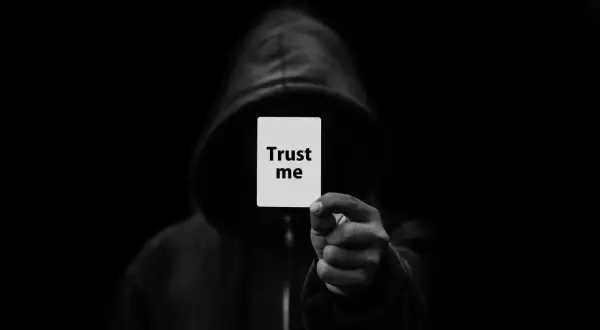 Postać w kapturze trzyma kartkę z napisem "Trust me". Czy można jej zaufać? 286 kk.