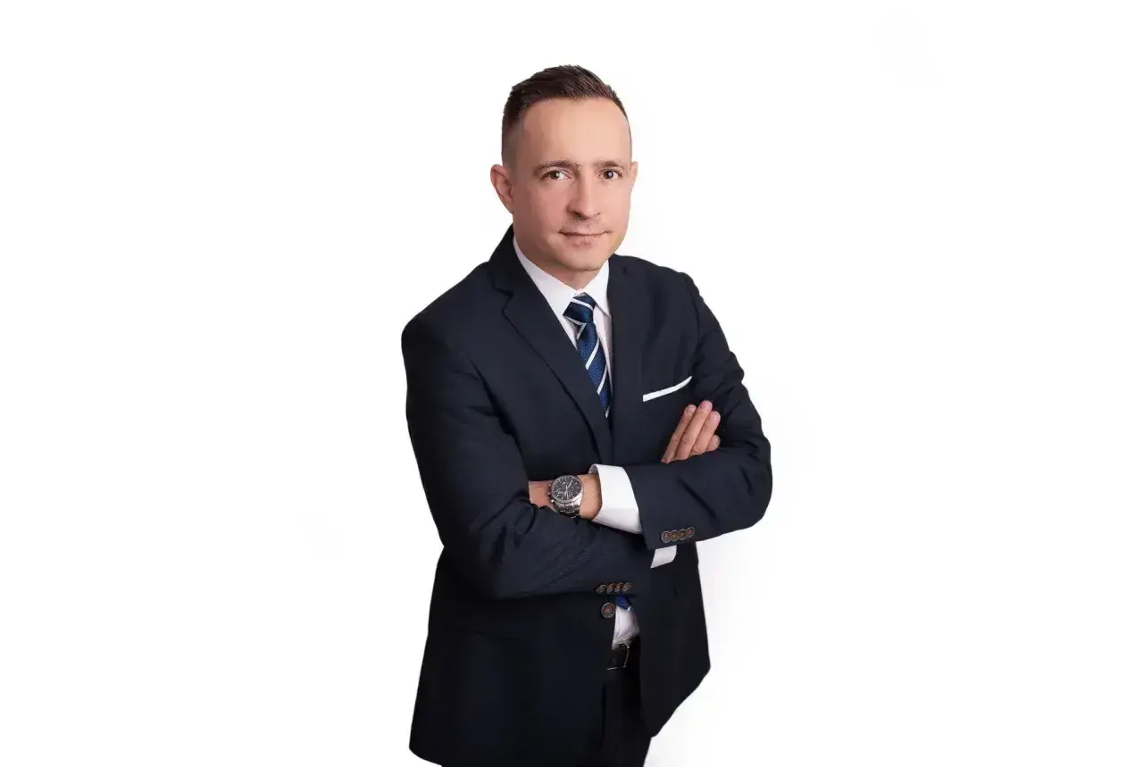 Mężczyzna w garniturze ze skrzyżowanymi rękami na białym tle.