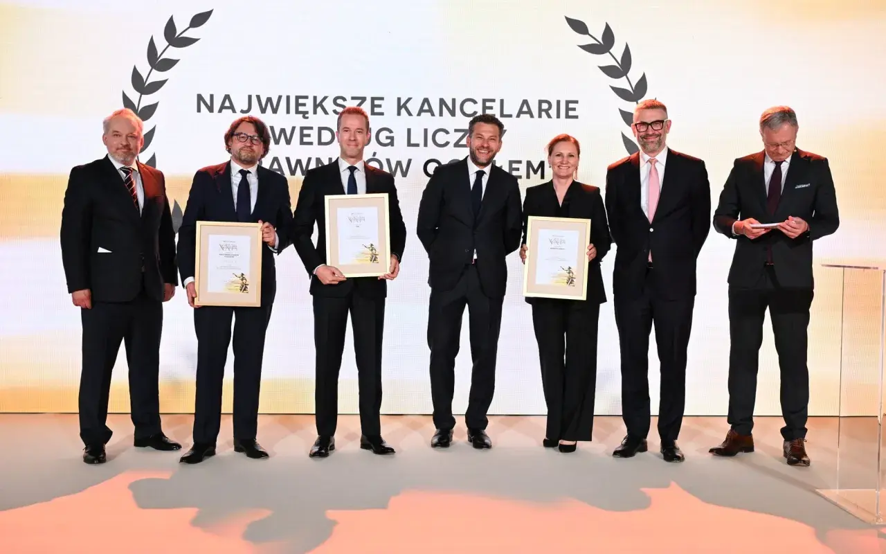 Sześć osób w garniturach odbiera nagrody na scenie.
