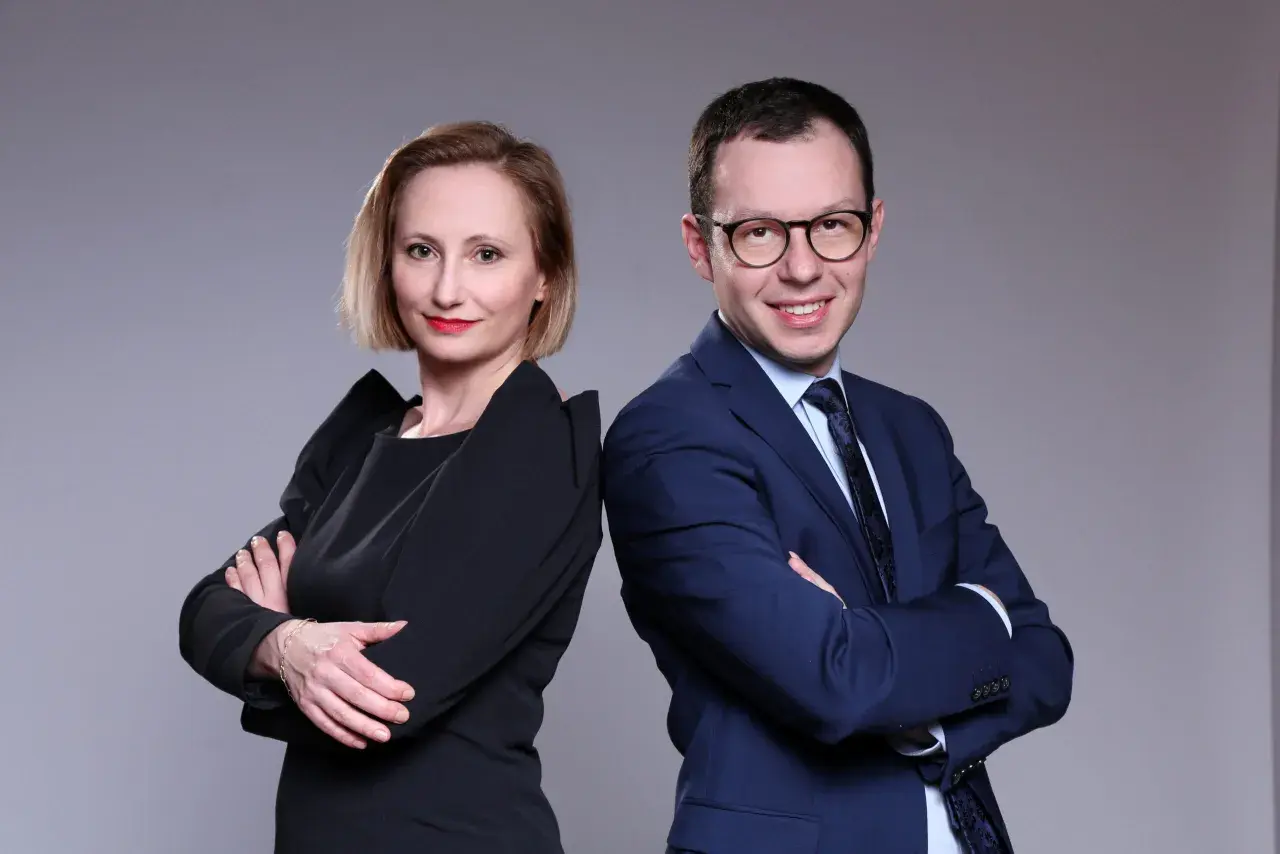 Kobieta i mężczyzna w strojach biznesowych stoją plecami do siebie, patrząc w stronę widza.