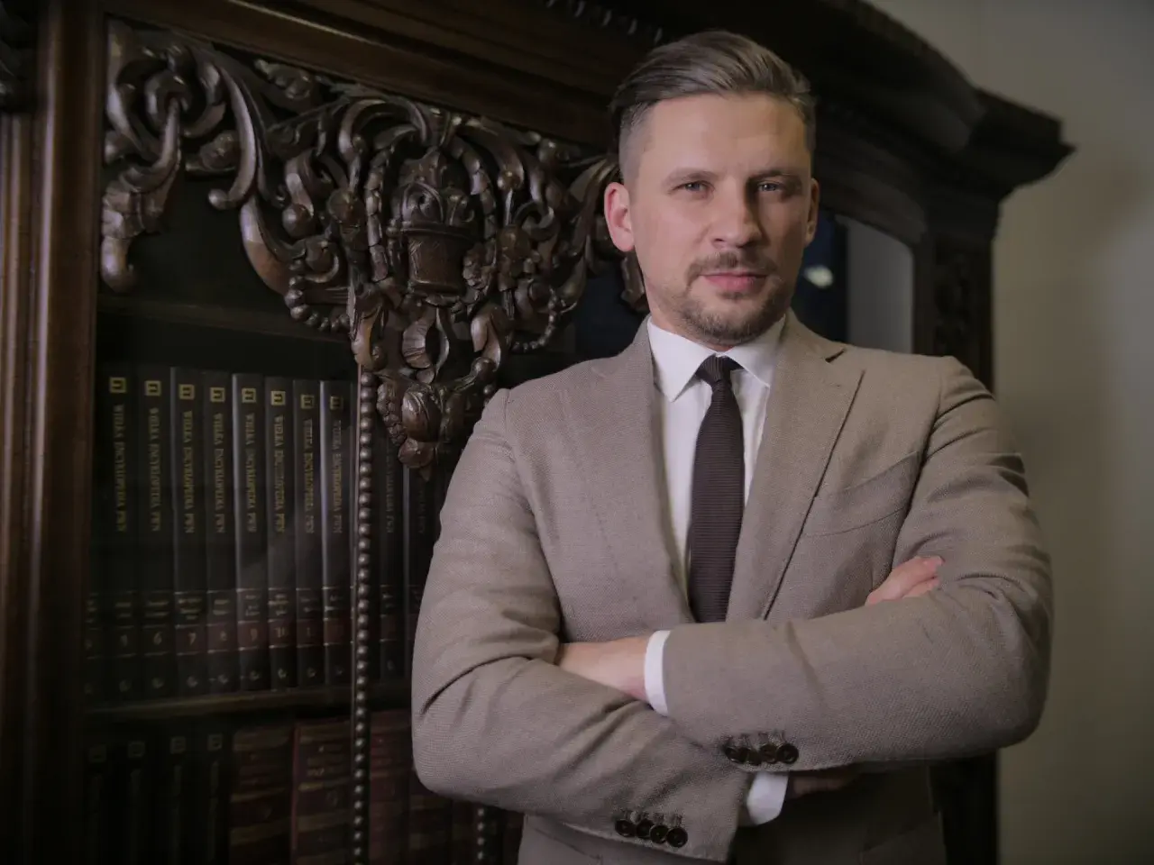 Mężczyzna w garniturze stoi przed regałem z książkami.