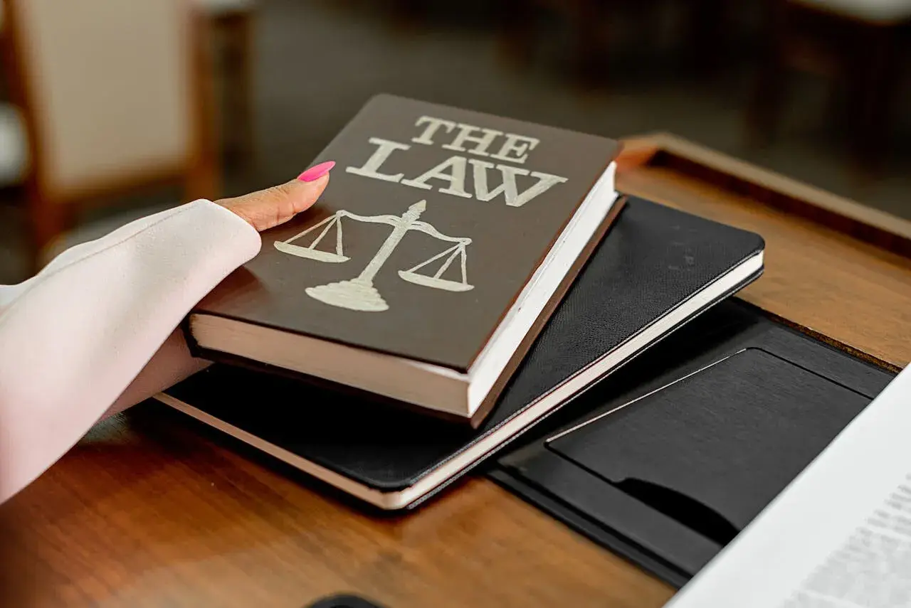 Dłoń z różowym lakierem na paznokciach trzyma książkę "The Law" z wagą sprawiedliwości. Może to symbolizować przygotowanie do wydania wyroku łącznego.