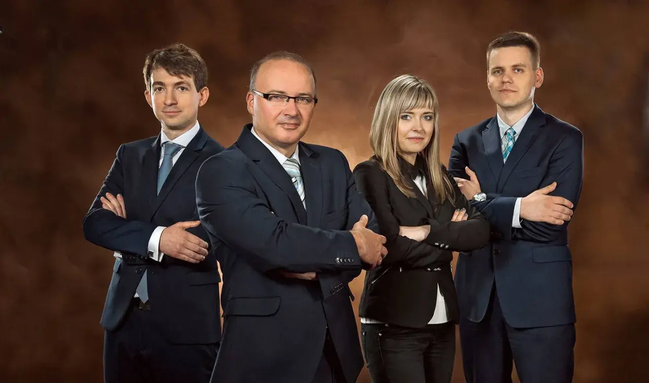 Cztery osoby w garniturach stojące z rękami skrzyżowanymi na piersi.