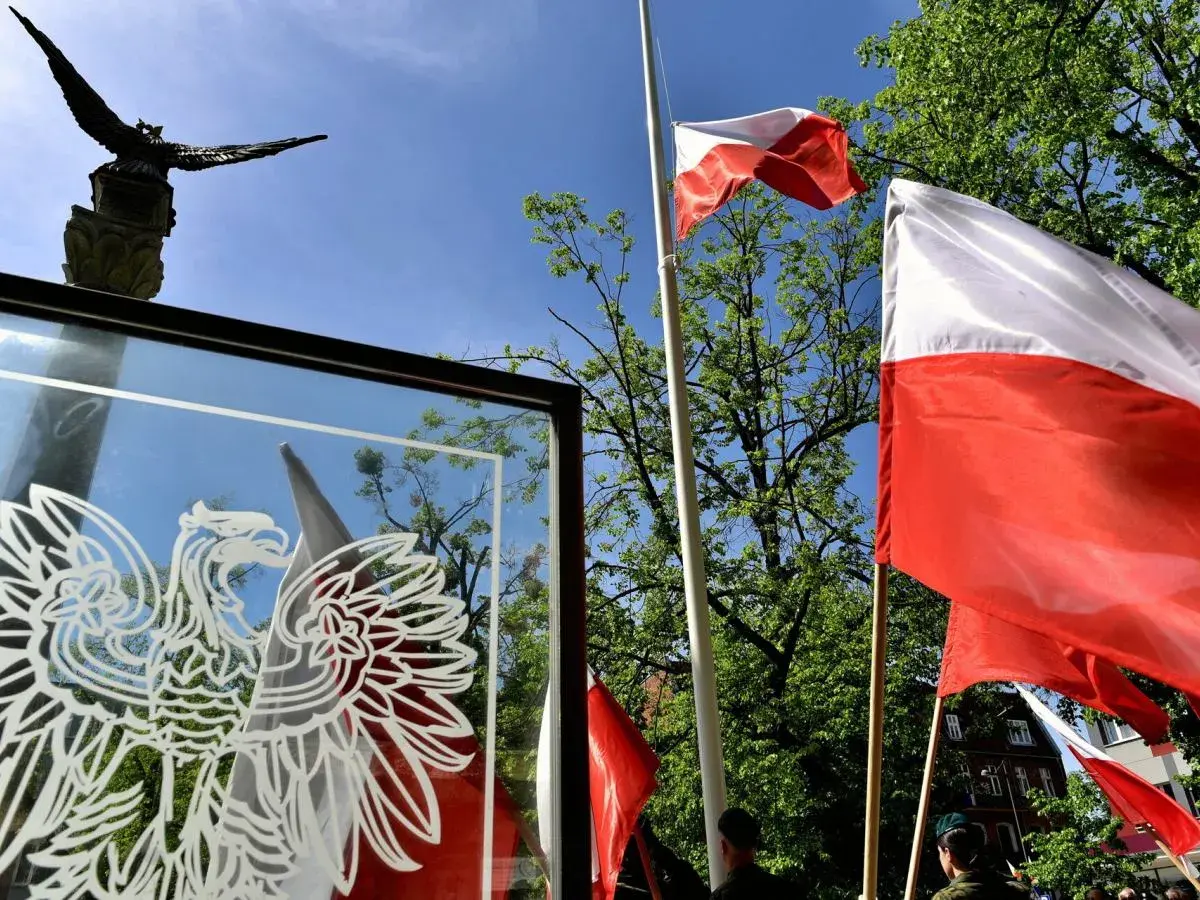 Orzeł biały i polskie flagi na tle nieba. Czy 3 maja można pracować? To pytanie zadają sobie Polacy w święto Konstytucji.