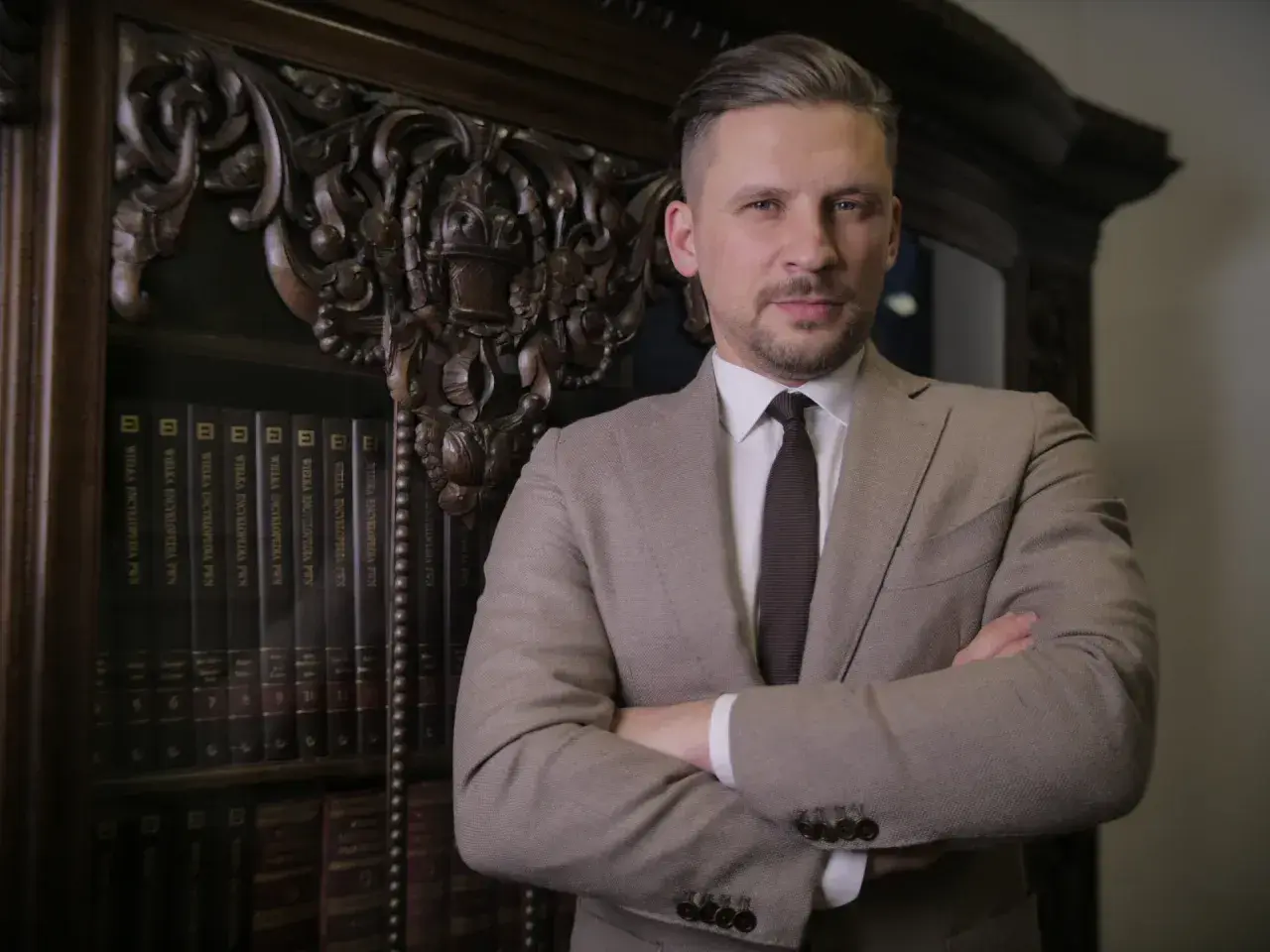 Mężczyzna w garniturze stoi przed regałem z książkami.