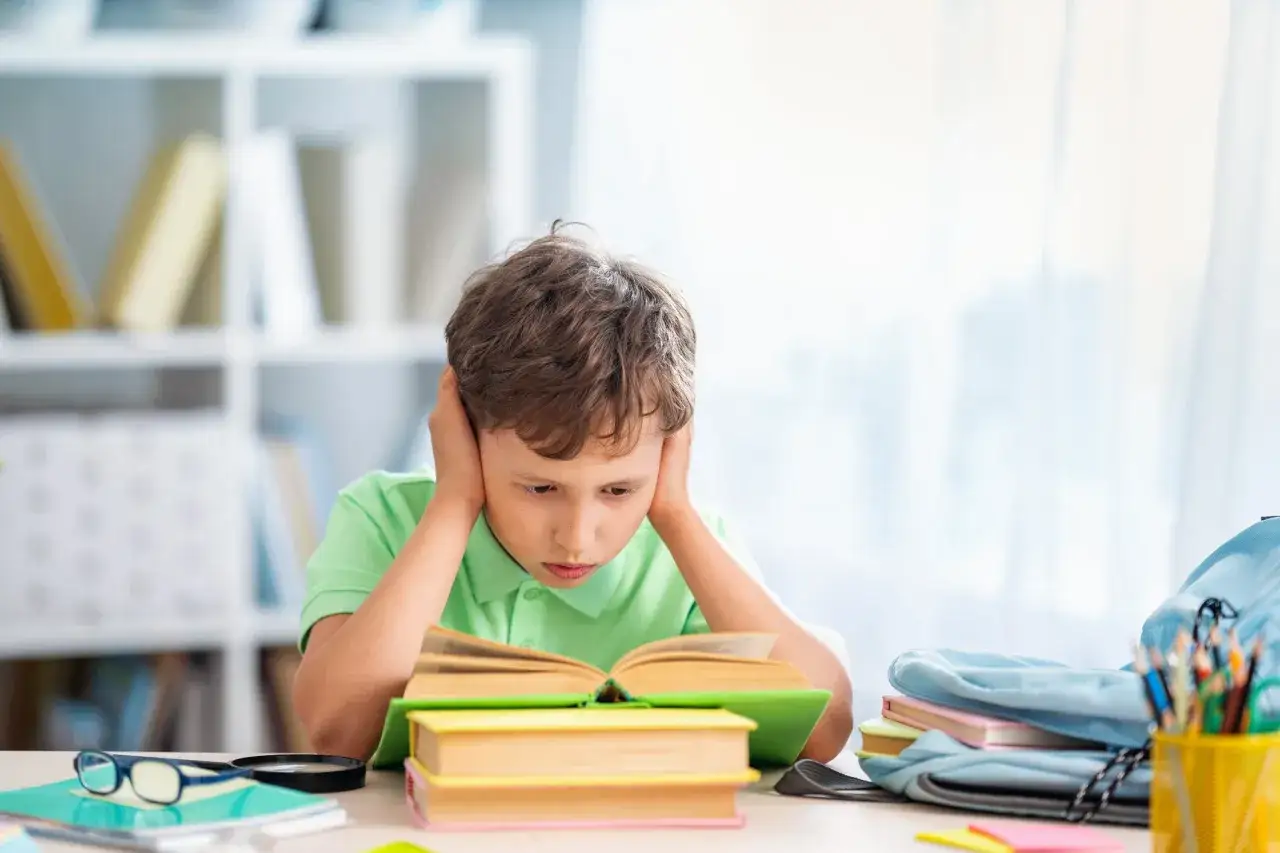 Chłopiec z dysleksją rozwojową z trudem czyta książkę, trzymając się za uszy.