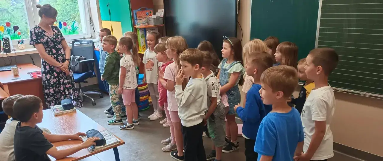 Nauczycielka z klasą dzieci, które słuchają jej uważnie. Czy zerówka jest obowiązkowa? Dzieci w wieku przedszkolnym i wczesnoszkolnym w sali lekcyjnej.