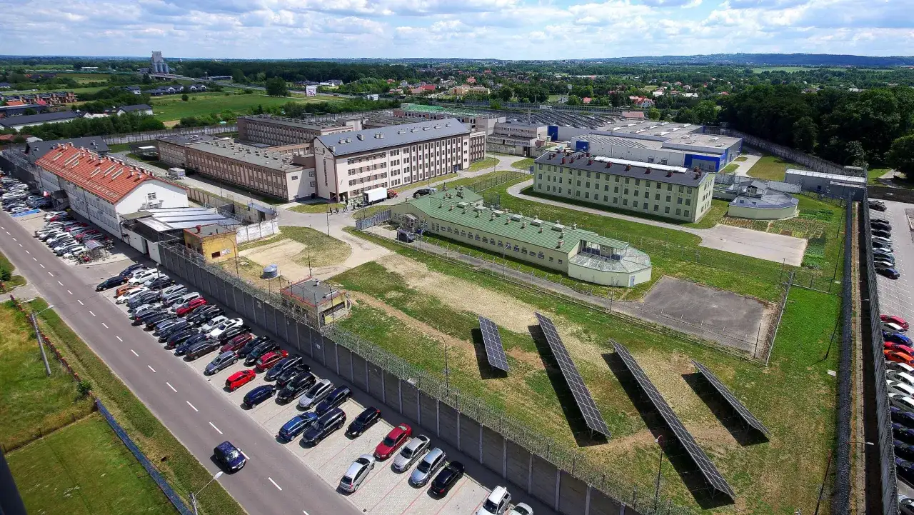 Widok z lotu ptaka na kompleks budynków o charakterze penitencjarnym, otoczony wysokim murem z drutem kolczastym.