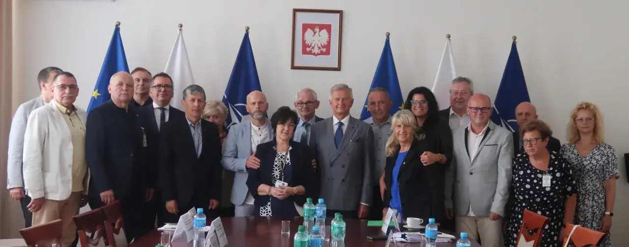 Grupa osób pozuje do zdjęcia na tle flag. Widać, że to spotkanie przedstawicieli związku zawodowego.