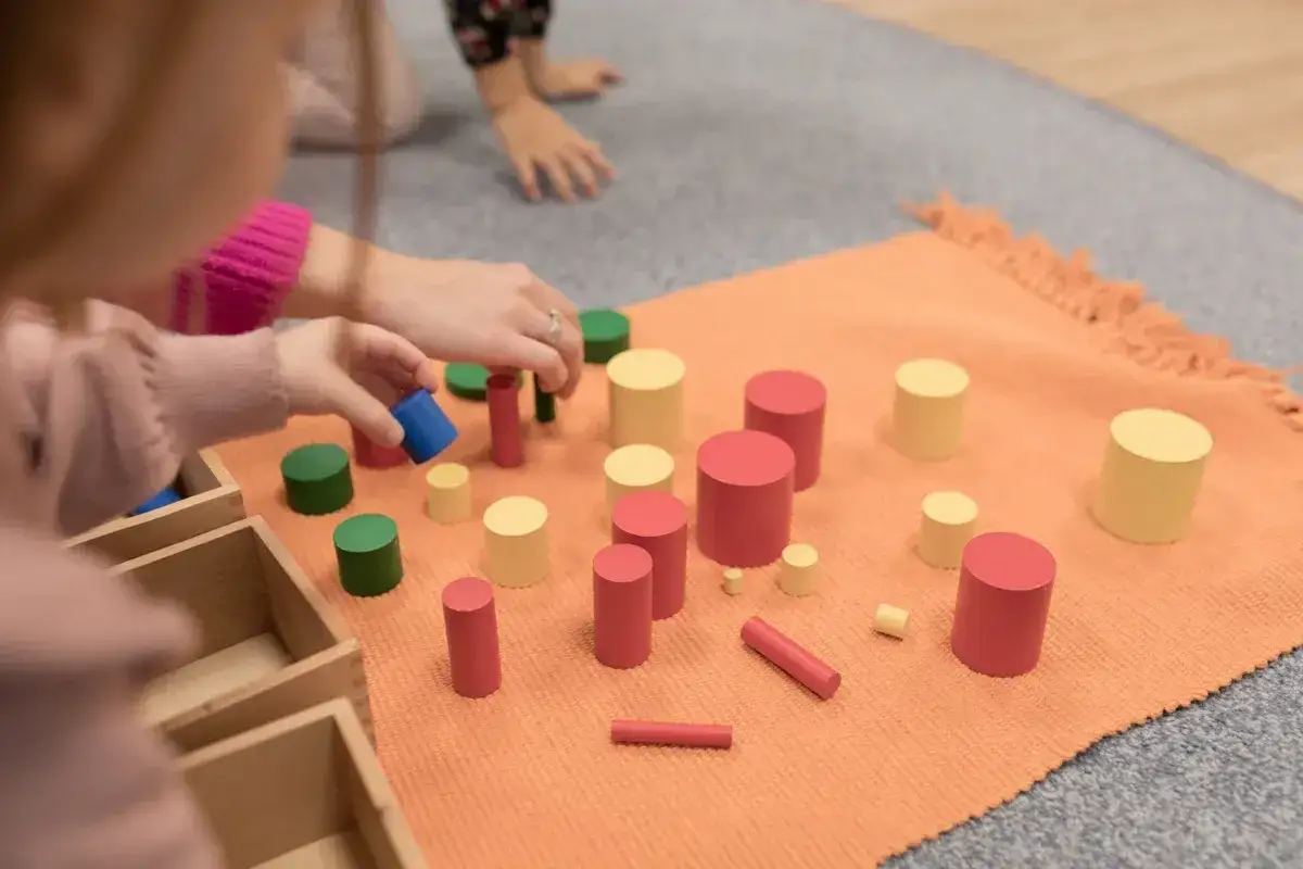 Dzieci bawią się kolorowymi walcami, ćwicząc koordynację i percepcję wzrokową. To nauka przez zabawę, zgodna z metodą Montessori.