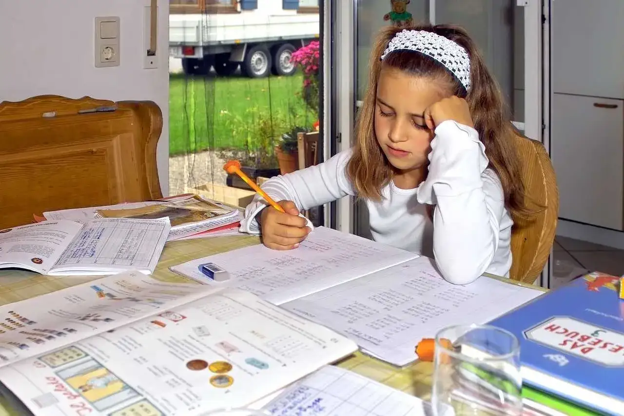 Dziewczynka pochłonięta nauką w domu, typowy obrazek z homeschoolingu. Wokół zeszyty, książki i ołówek.