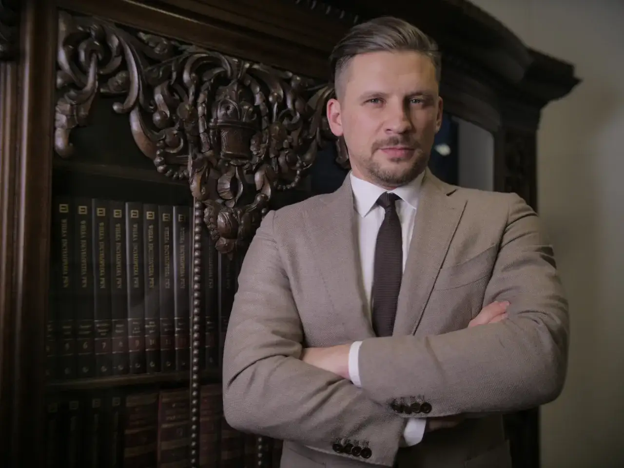 Mężczyzna w garniturze stoi przed regałem z książkami.