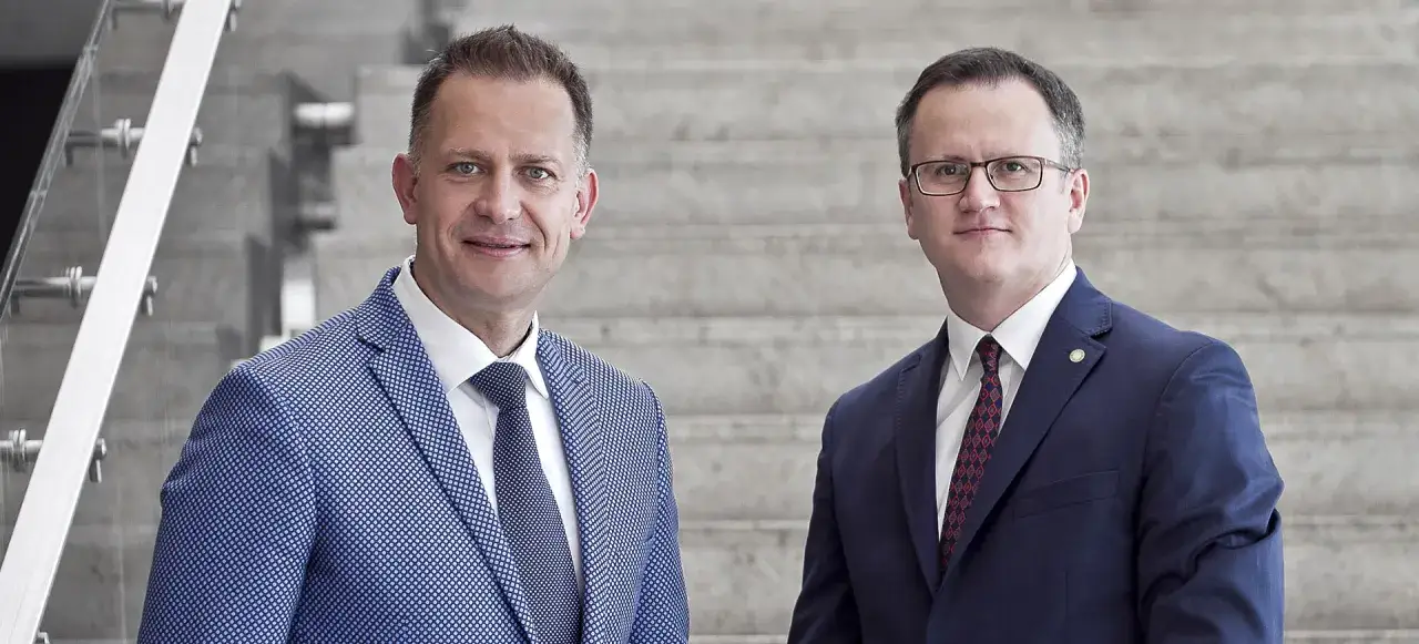 Dwóch mężczyzn w garniturach stoi na tle schodów.