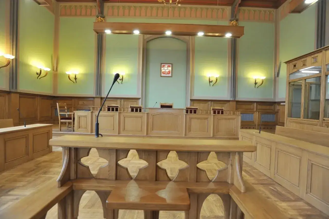Pusta sala sądowa, gotowa na apelację od wyroku. Drewniane ławy, mównica i godło państwowe tworzą uroczystą atmosferę.