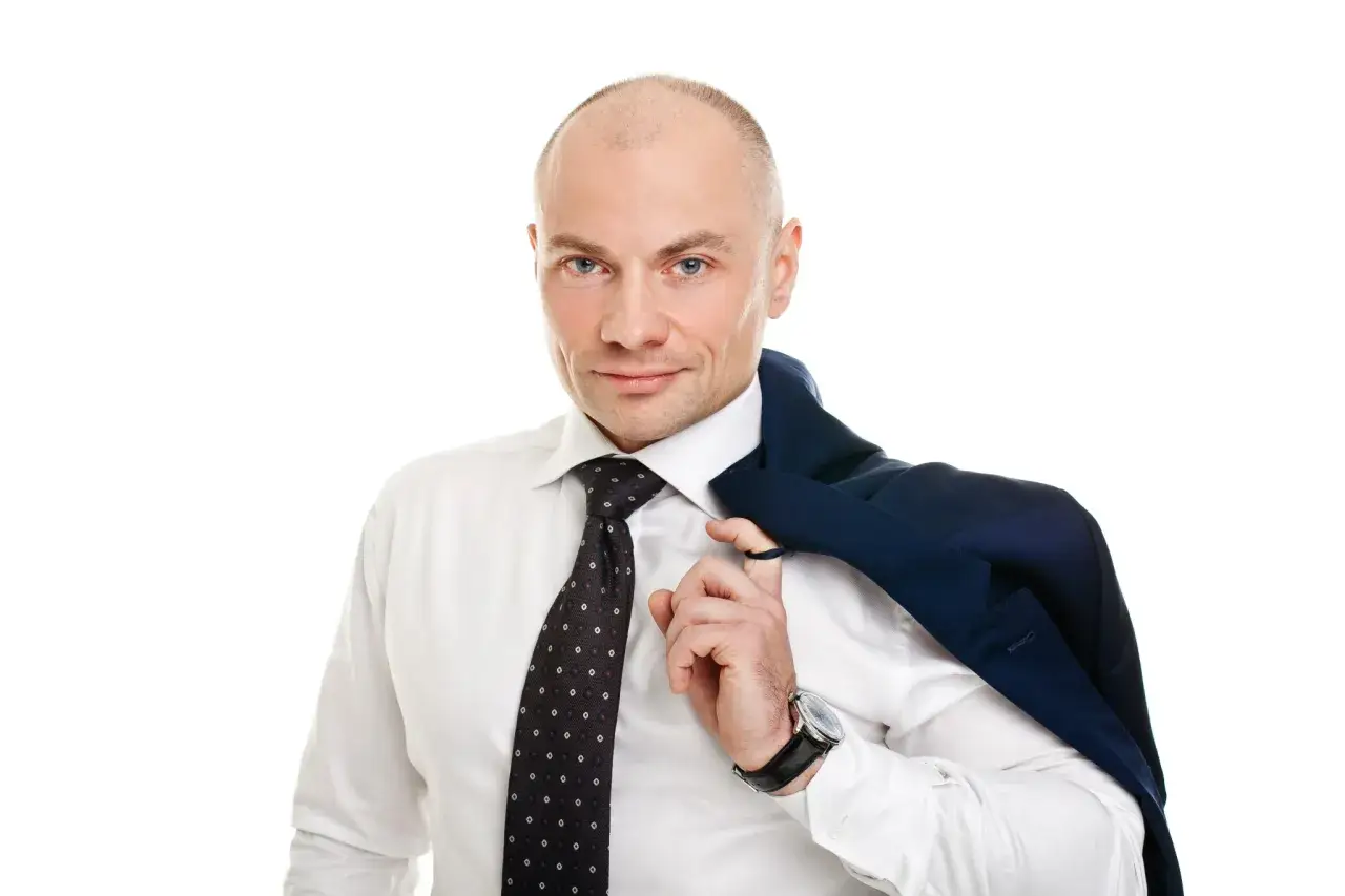 Łysy mężczyzna w białej koszuli i krawacie, z marynarką na ramieniu.