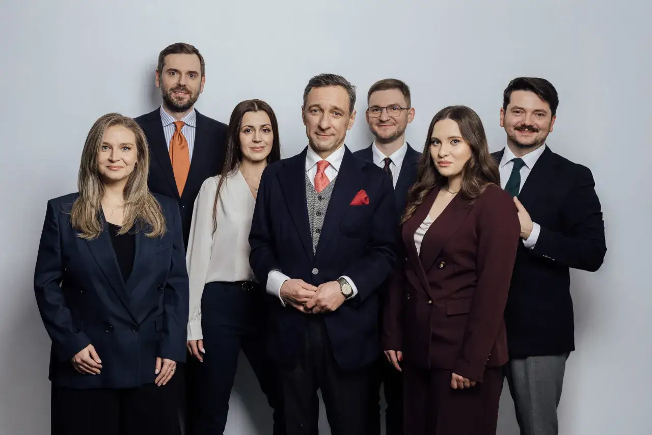 Grupa zawodowców w garniturach i kostiumach pozuje do zdjęcia na jasnym tle.