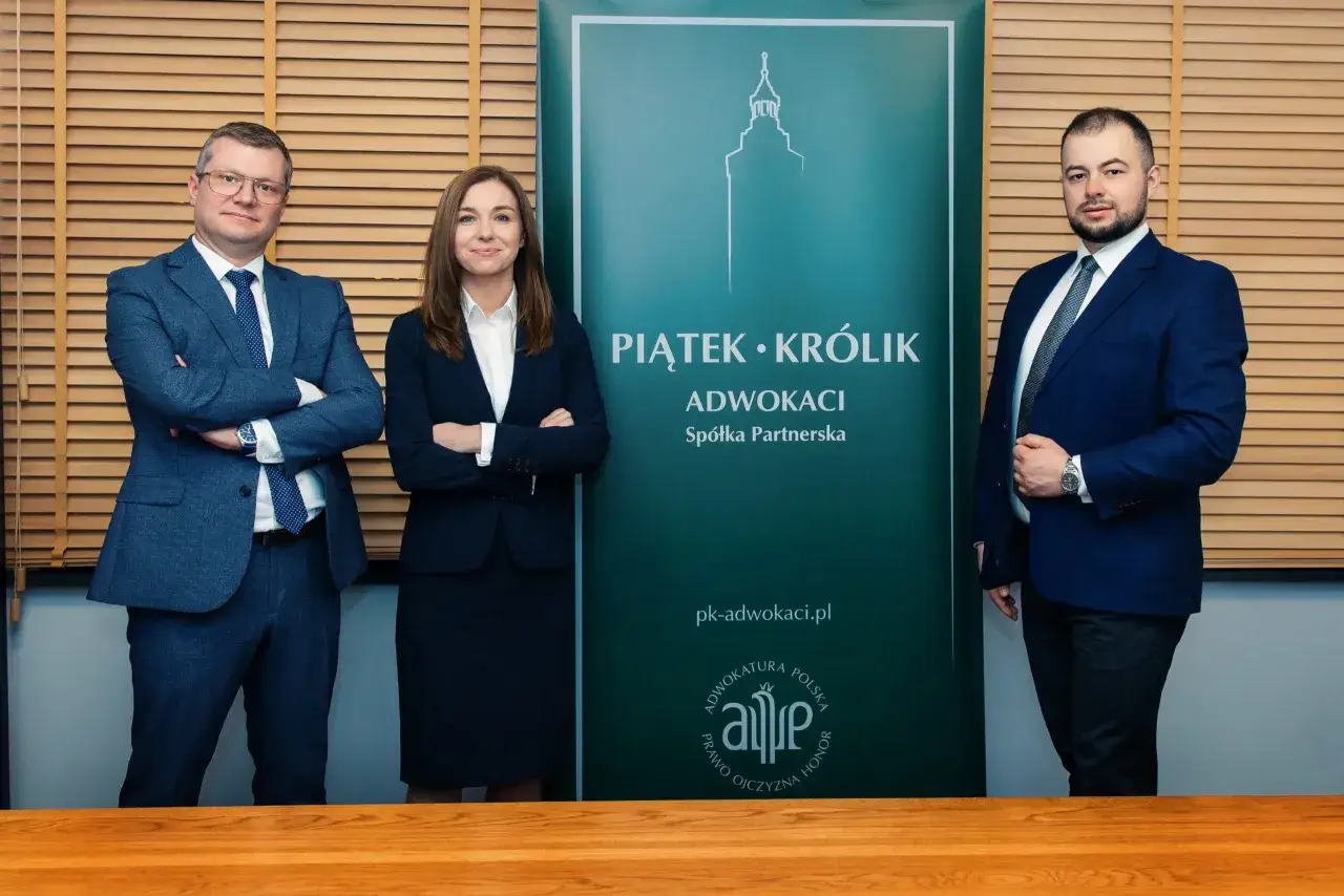 Trzech prawników w garniturach stoi przed zielonym banerem kancelarii.