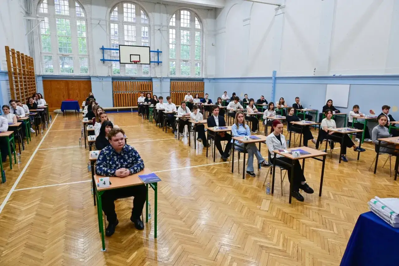 Uczniowie siedzą w ławkach w sali gimnastycznej, skupieni na zadaniach. To ważny dzień – egzamin dojrzałości.