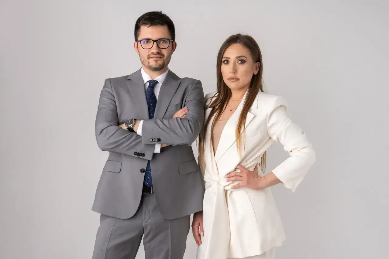 Para prawników w garniturach, mężczyzna z rękami skrzyżowanymi na piersi, kobieta z ręką na biodrze.