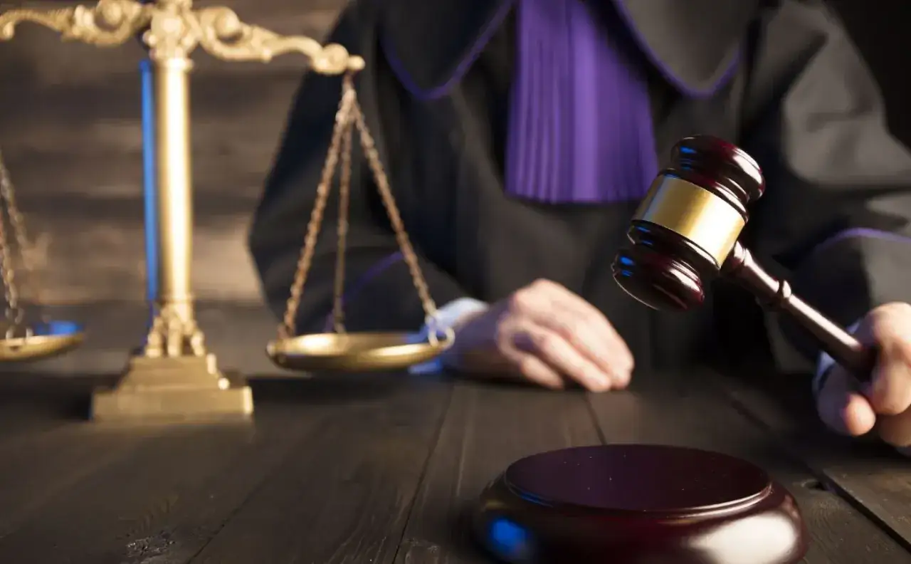 Sędzia w todze z purpurową żabotą trzyma młotek, obok waga sprawiedliwości. Symbolika prawa rodzinnego.