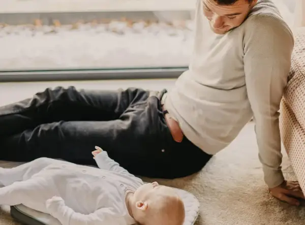 Mężczyzna patrzy na dziecko leżące na dywanie. Czy to jego syn? Zaprzeczenie ojcostwa wisi w powietrzu.