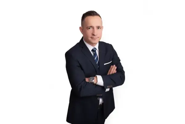 Mężczyzna w garniturze ze skrzyżowanymi rękami na białym tle.