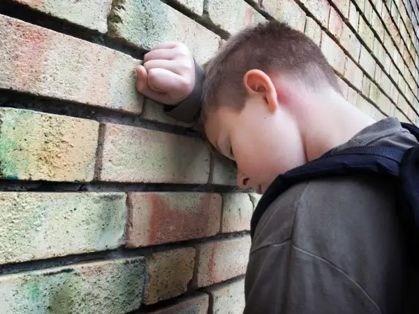 Chłopiec z plecakiem opiera głowę o ceglaną ścianę, wyrażając smutek i poczucie osamotnienia, które mogą być objawami fobii szkolnej.