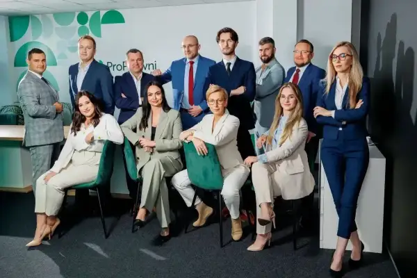 Grupa profesjonalistów w garniturach pozuje do zdjęcia w nowoczesnym biurze.