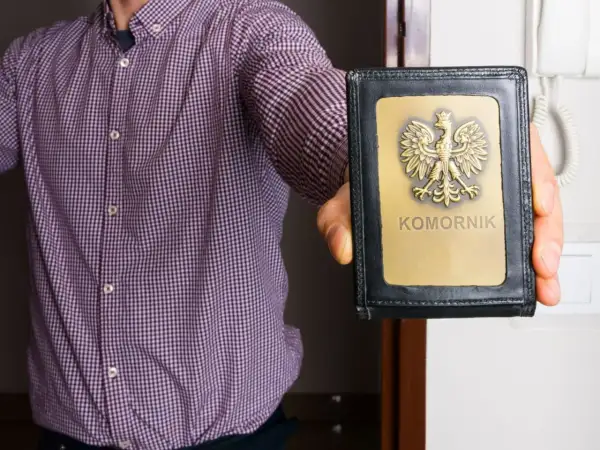 Mężczyzna w koszuli prezentuje legitymację z orłem i napisem "KOMORNIK". Może to oznaczać egzekucję komorniczą.