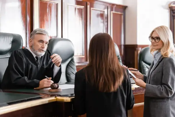 Sędzia w todze słucha zeznań, gdy prawniczka notuje. Rozprawa sądowa w toku.